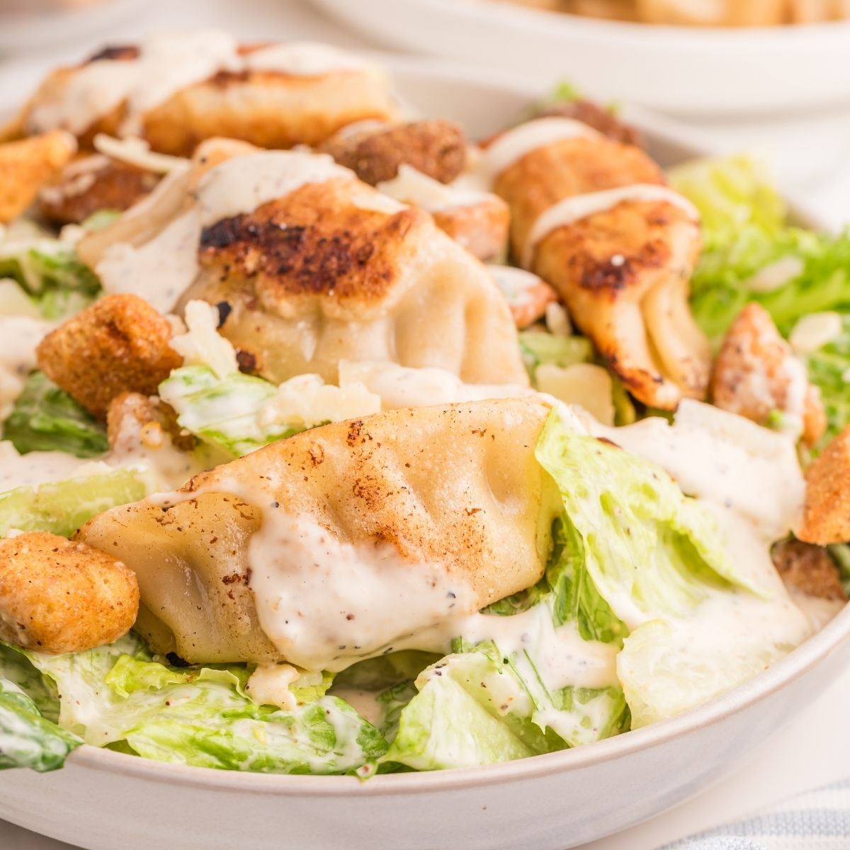 Bowl of Caesar salad topped with potstickers.