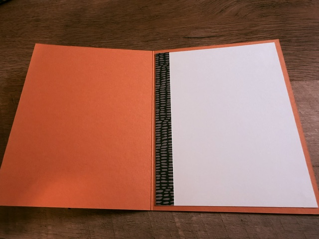 An open greeting card with an orange interior and a blank white space on the right, featuring a black patterned edge.