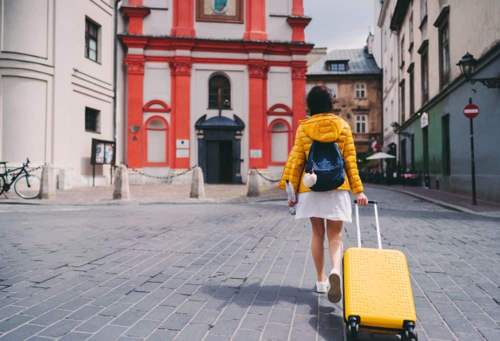 Rear view of woman with suitcase and umbrella strolling among colourful buildings.