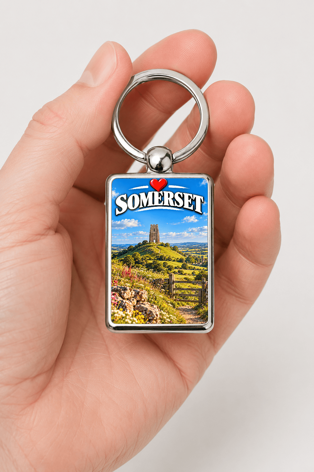 Hand holding polished metal Somerset keyring with Glastonbury Tor landscape, heart detail and "Somerset" wording souvenir