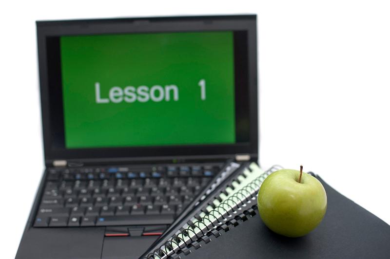Learning via the computer concept with a spiral bound notebook and fresh green apple in front of a laptop screen reading LESSON 1
