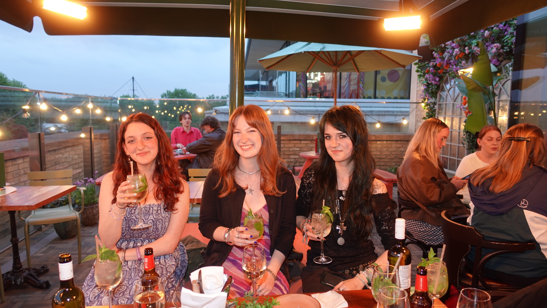 Three women have cocktails on a rooftop bar.