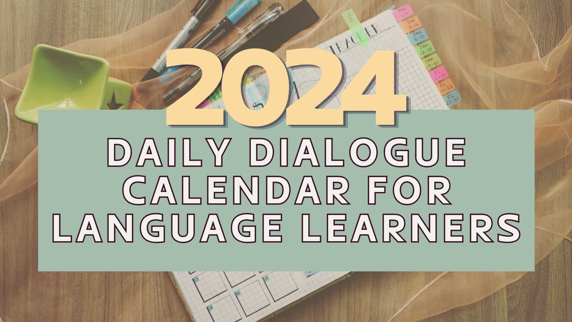 Calendar labeled "2024 Daily Dialogue Calendar for Language Learners" on a wooden table with pens, a green dish, and fabric.