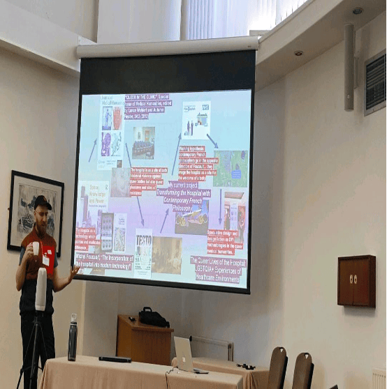 Image of a man standing in front of a screen with a slide exploring zine-making.