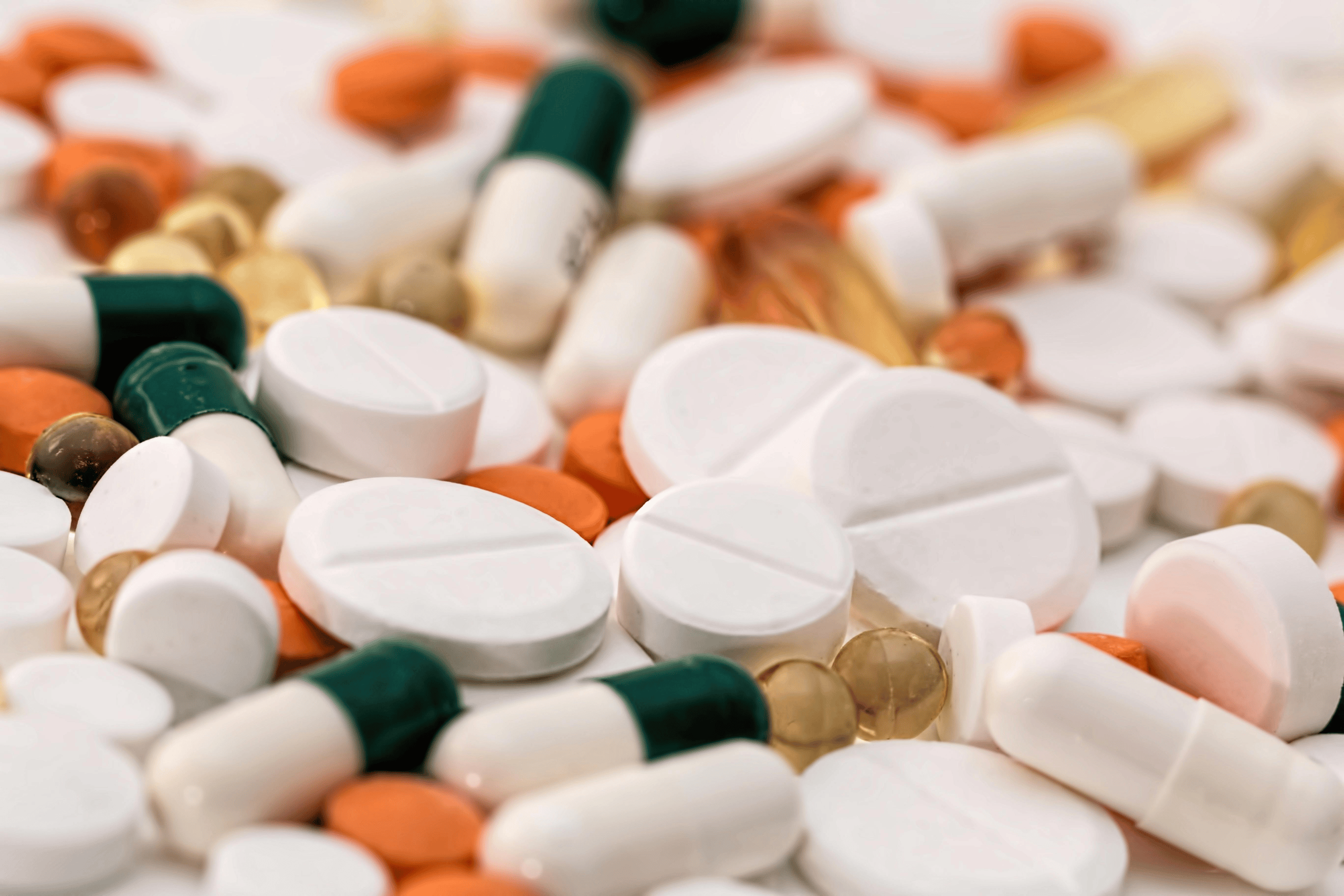 Close up photograph of pharmaceutical pills. Some in black and white caps, some round and white, and others white and orange.