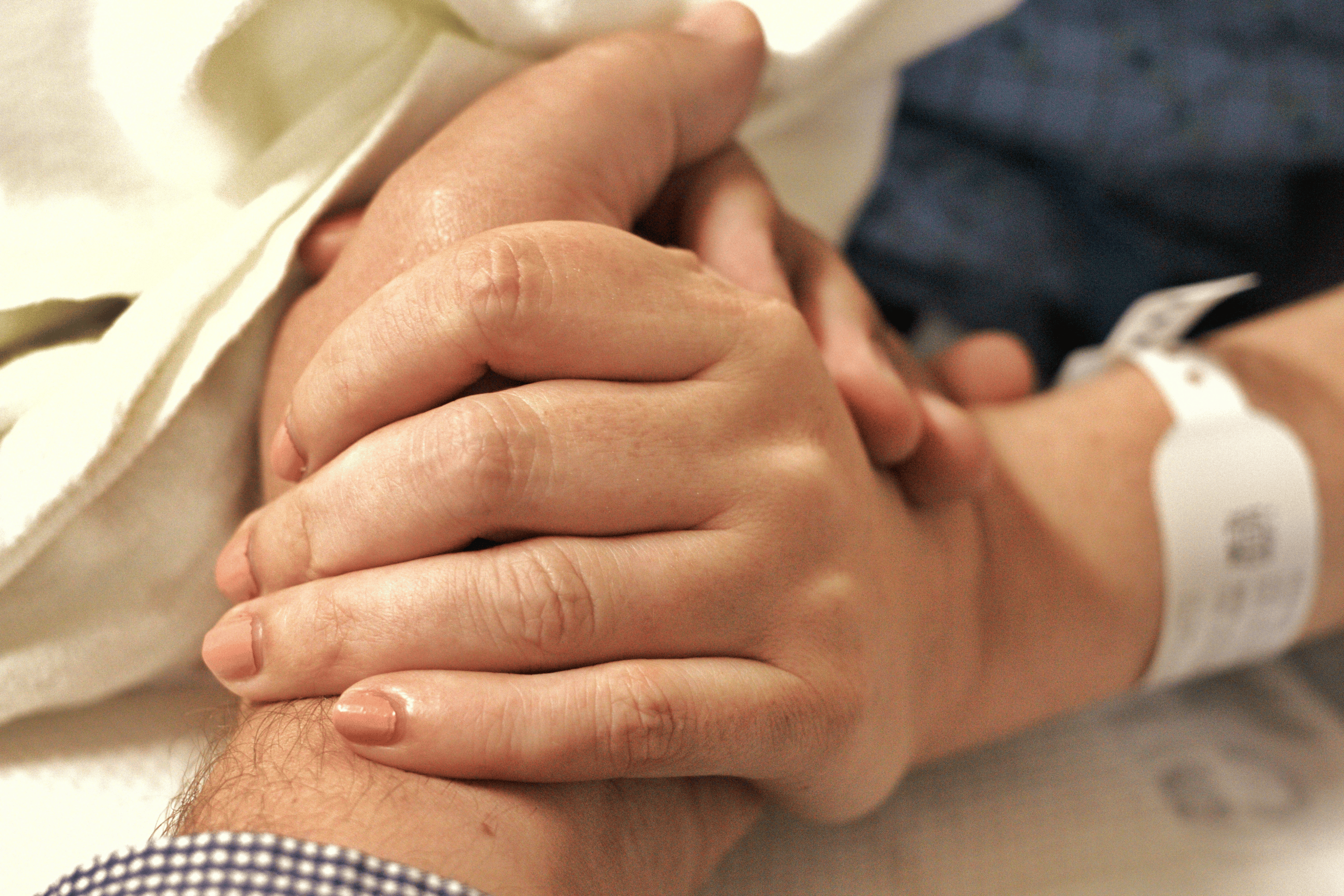 Zoomed in photograph of two hands clasping, one with a hospital tag round the wrist.