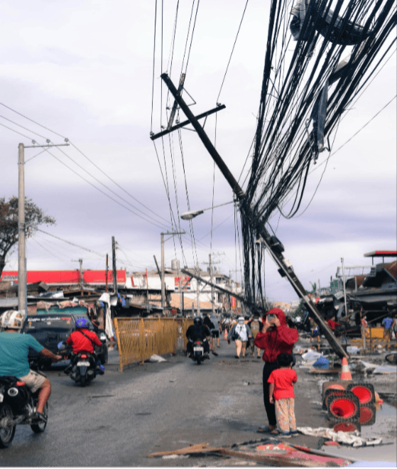 Image of the aftermath of a hurricane or some other natural disaster with telephone pole falling down and people on the street.