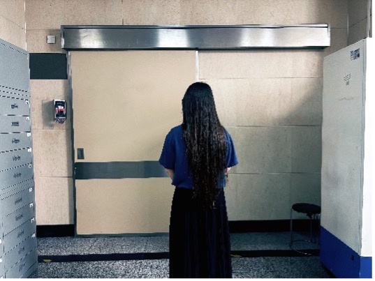 A person with long black hair standing outside a hospital's ICU with the back facing the viewer