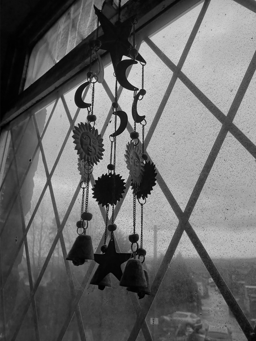 A black and white image of a window with wind chimes.