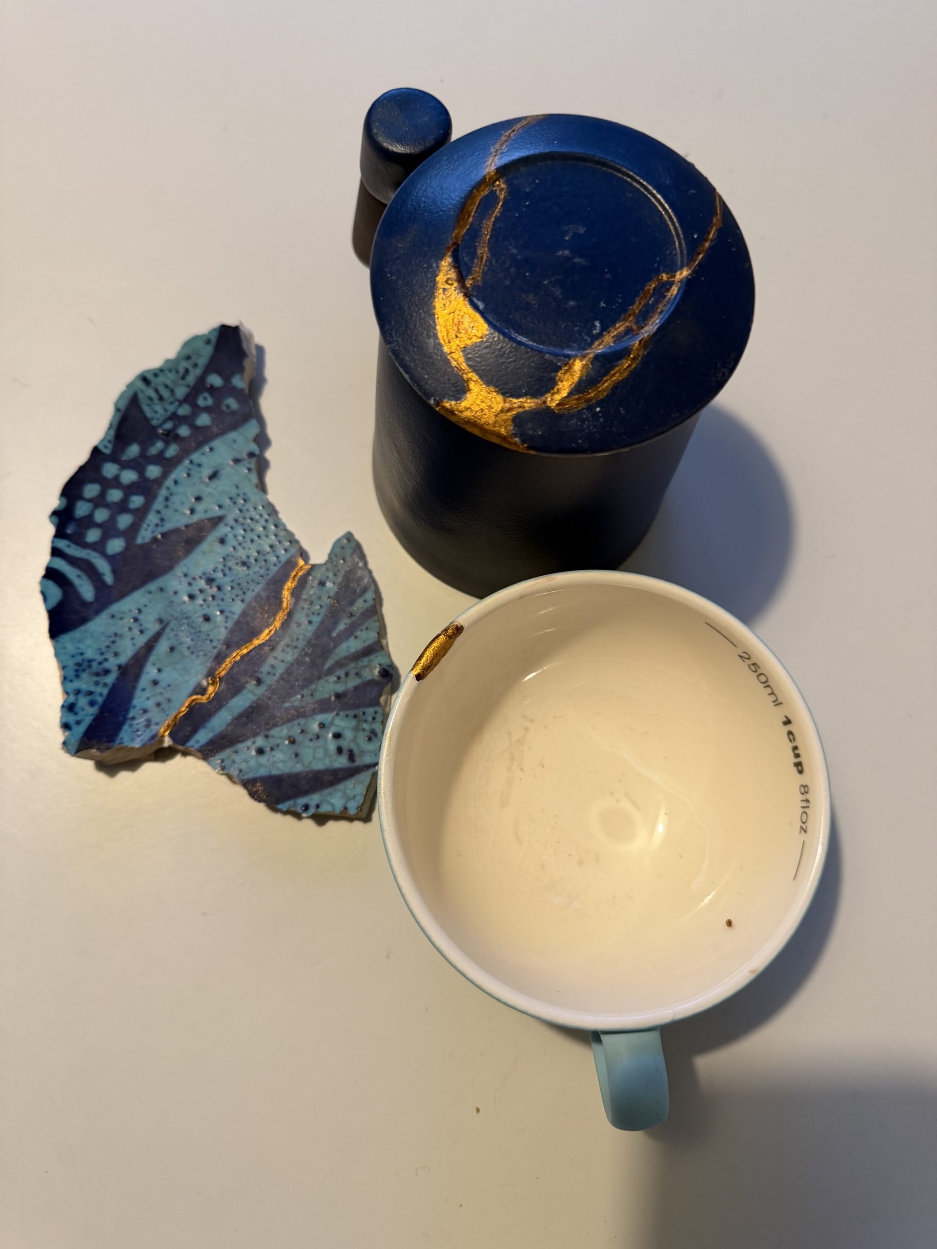 Photograph showing a collection of Kintsugi pottery. Each item of pottery is painted in blue tones, with the gold lines of the repairs standing out strikingly against the blue.