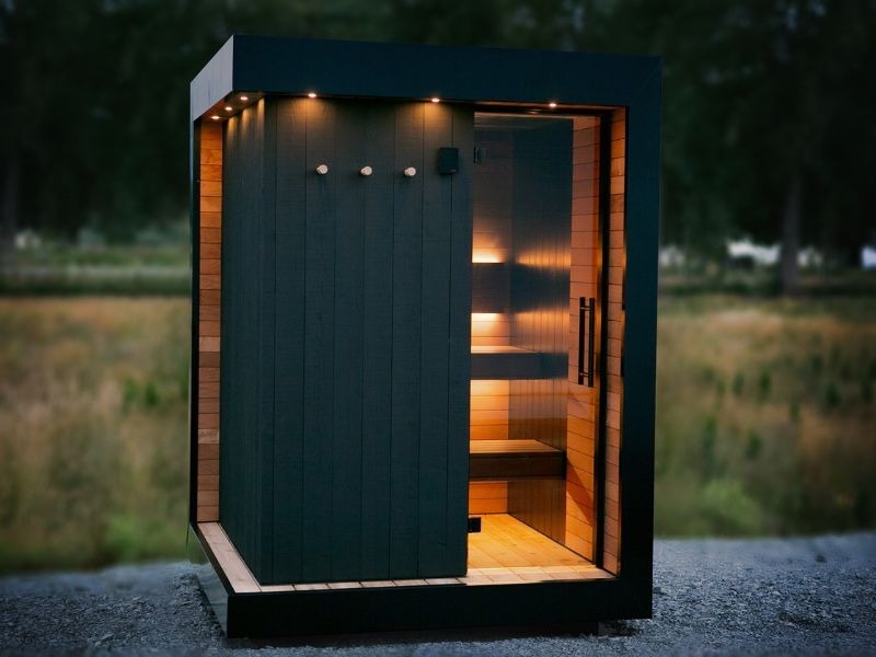 Modern black outdoor sauna with warm interior lighting in a private outdoor wellness space for a luxury Toronto home.