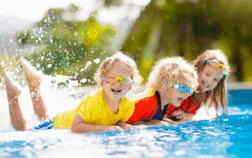 Three toddlers splashing and playing in a pool, enjoying sensory play as part of Summer OT activities for kids.