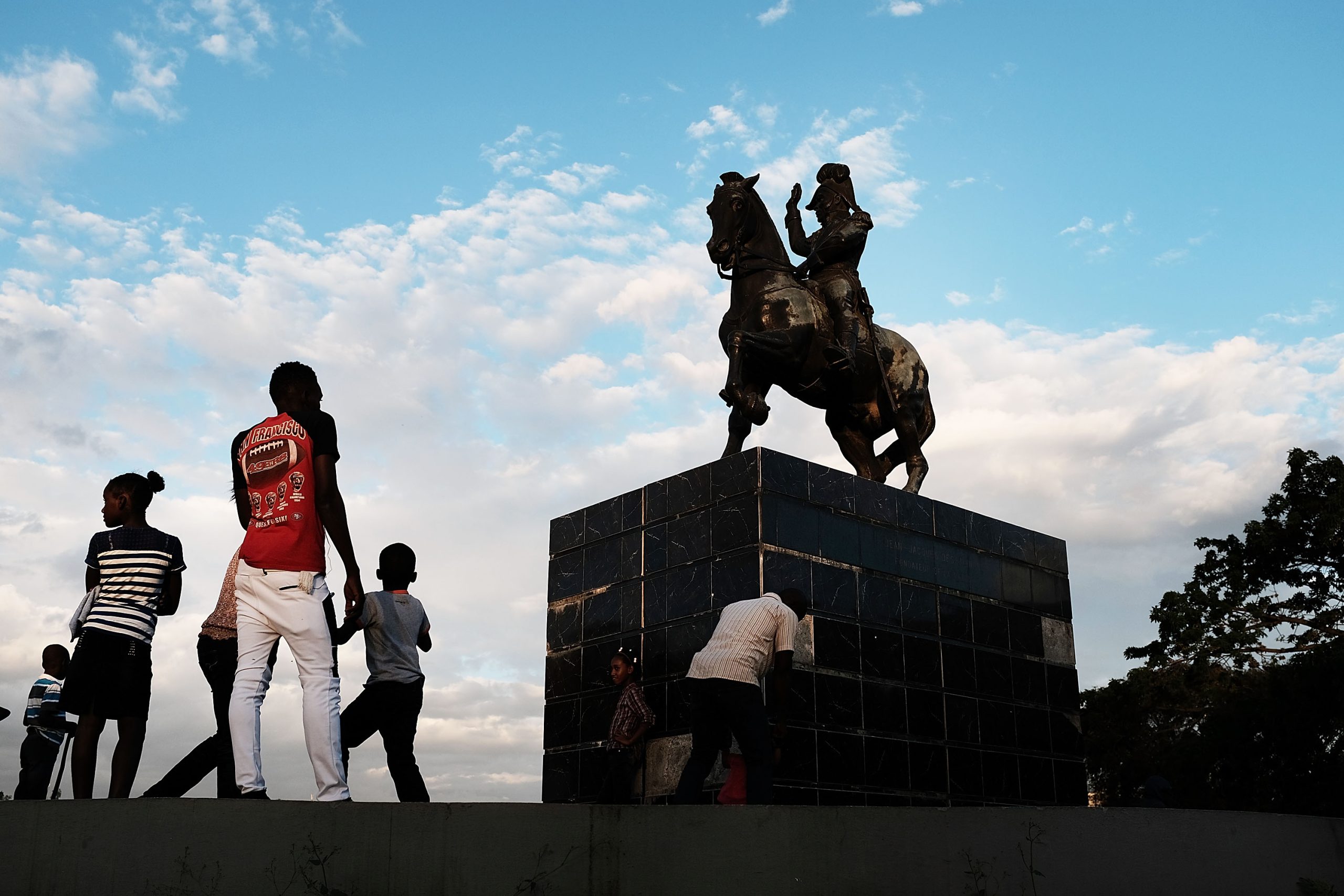 People stand under a statue of Jean-Jacques Dessalines, a leader of the Haitian Revolution and the first ruler of an independent Haiti, on February 10, 2018, in Port-au-Prince, Haiti. Photo by Spencer Platt/Getty Images.