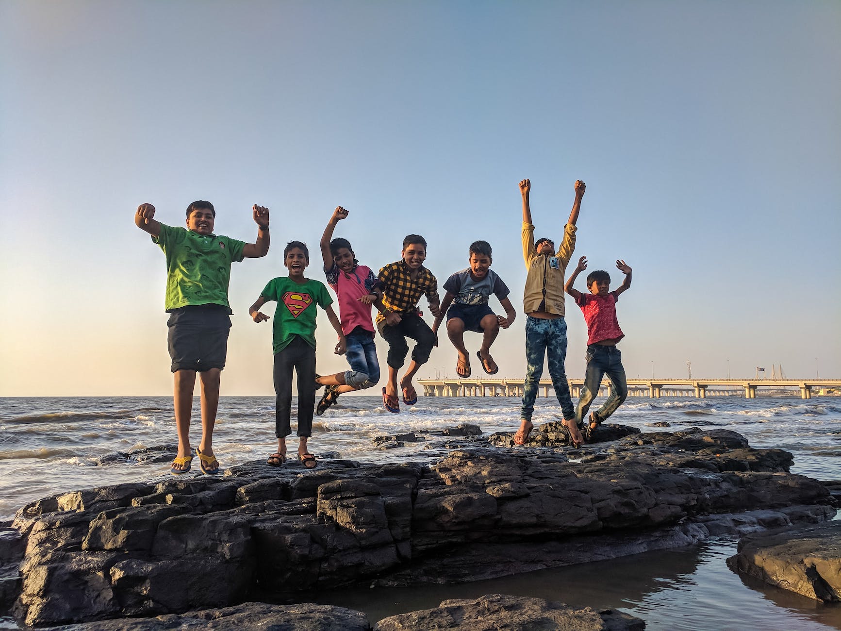 boy wearing green crew neck shirt jumping from black stone on seashore