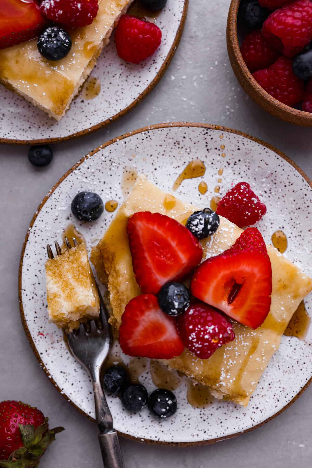 Sheet pan pancakes are not only soft and delicious, but the best way to feed a crowd! Serve them up with your favorite toppings for an unforgettable breakfast that's super easy to make! Top-down view of sheet pan pancakes topped with powdered sugar, syrup, and berries.