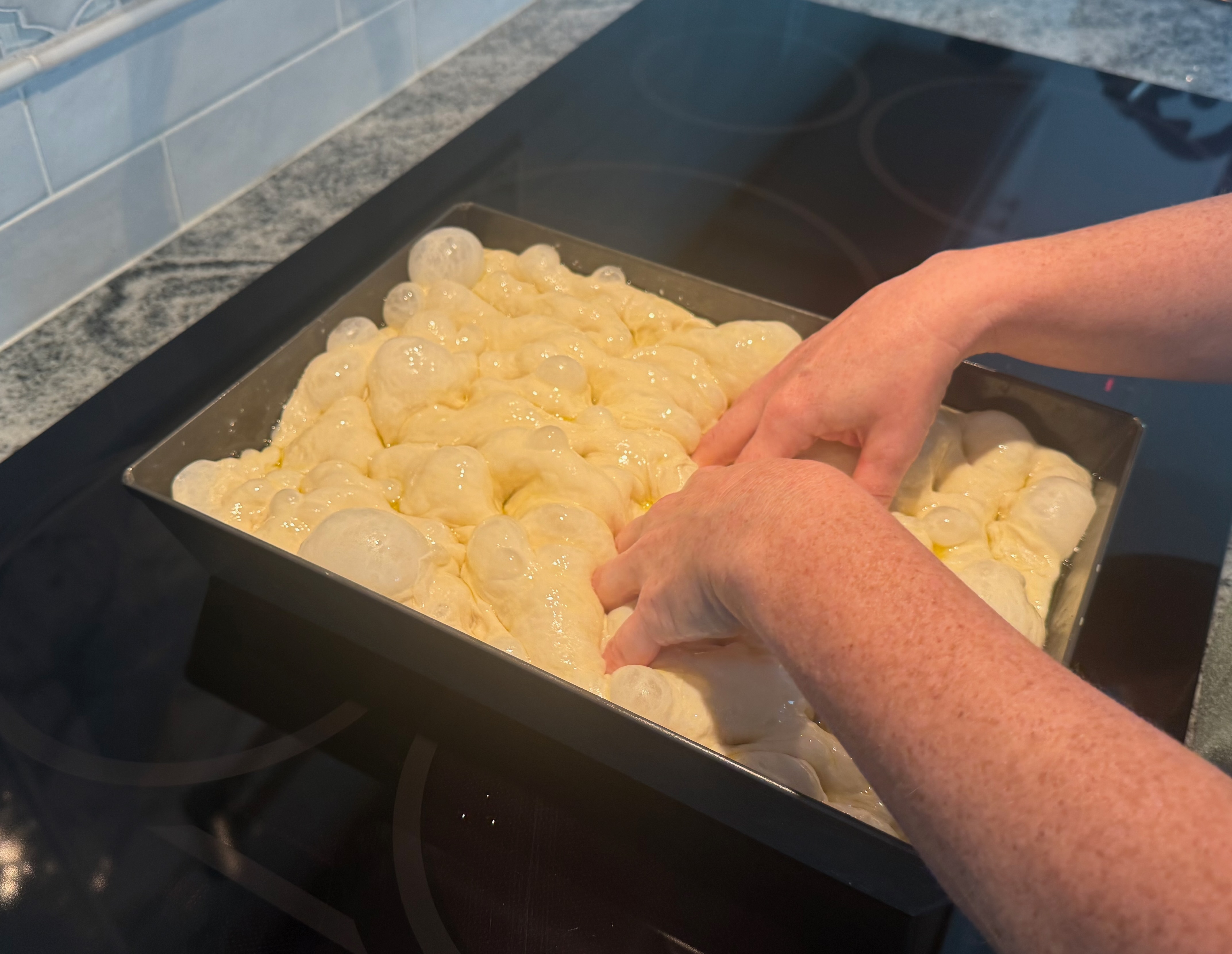 Dimpling focaccia dough with oiled fingers