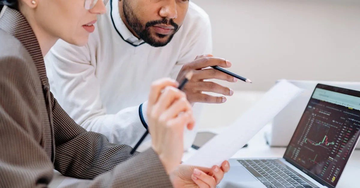 Two colleagues reviewing documents beside a laptop