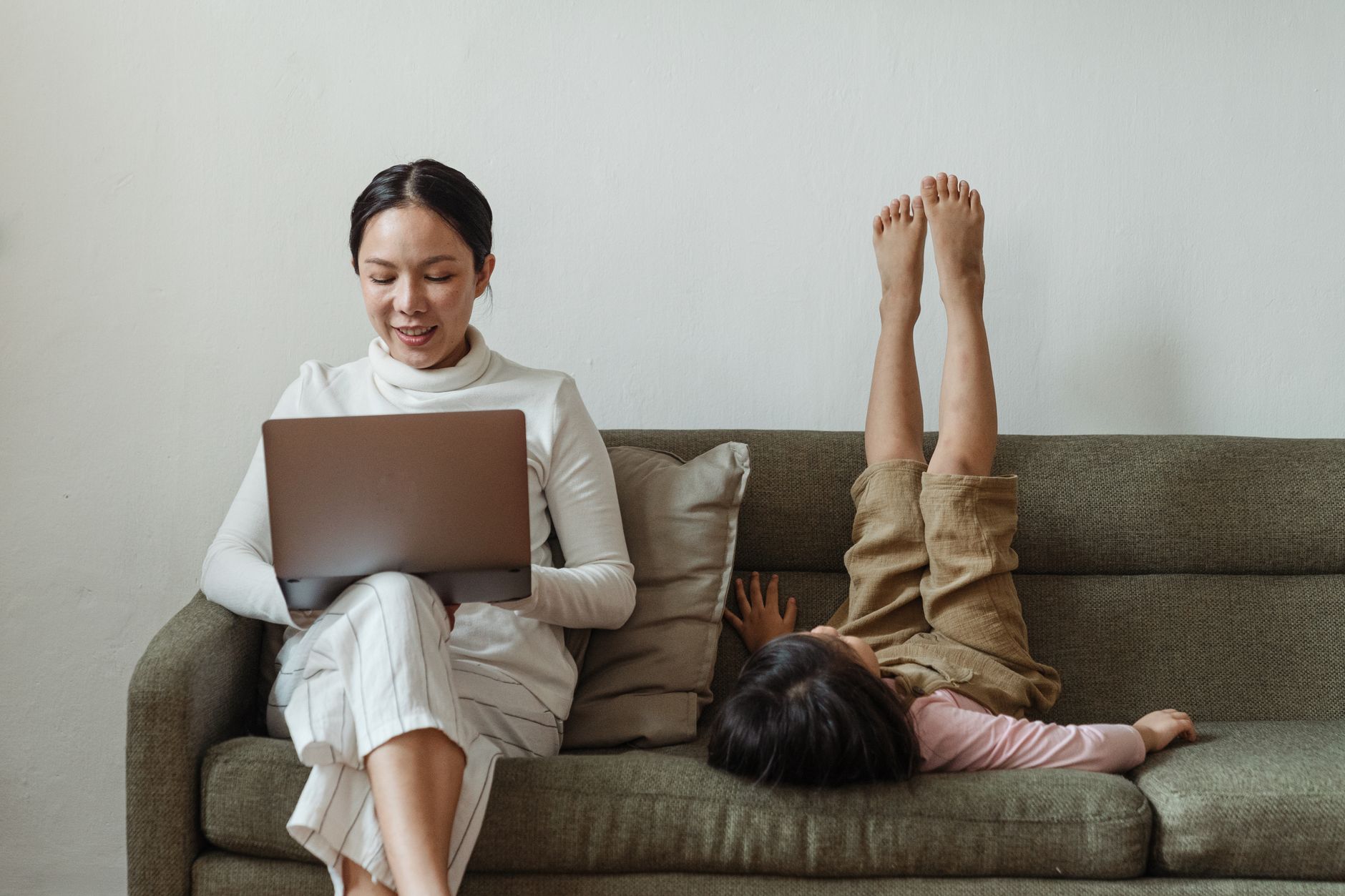 cheerful mother working on laptop near daughter on couch