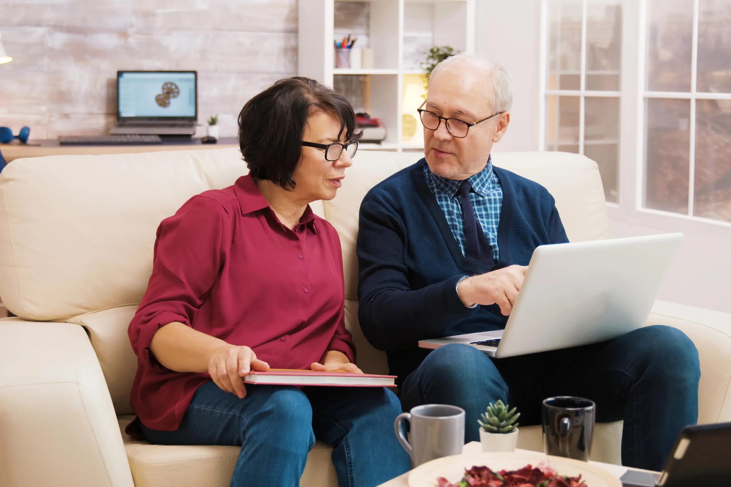 senior citizen couple using laptop while sitting on couch