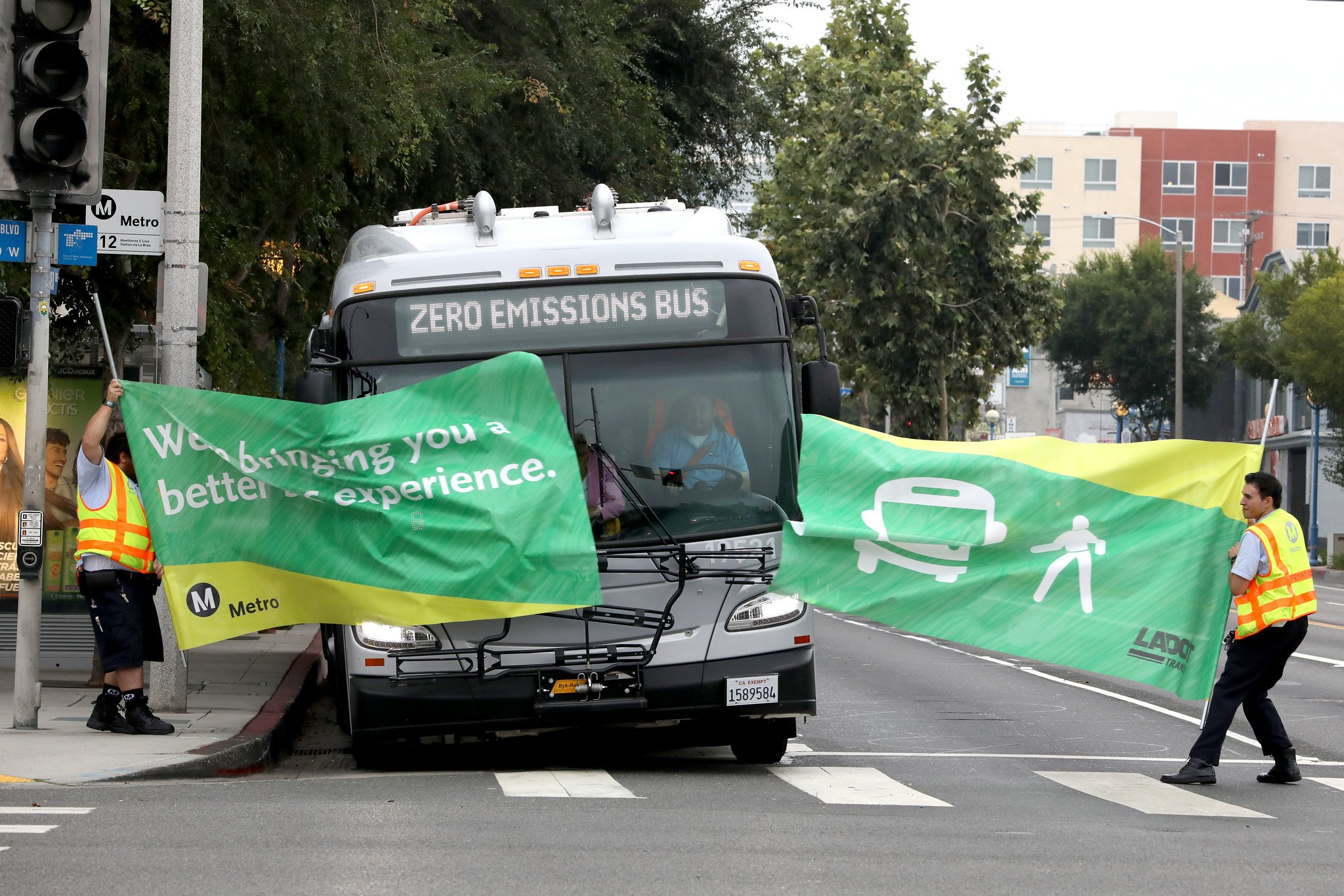 Photo of a Zero Emissions Bus breaking through a a green and yellow banner held by two metro workers