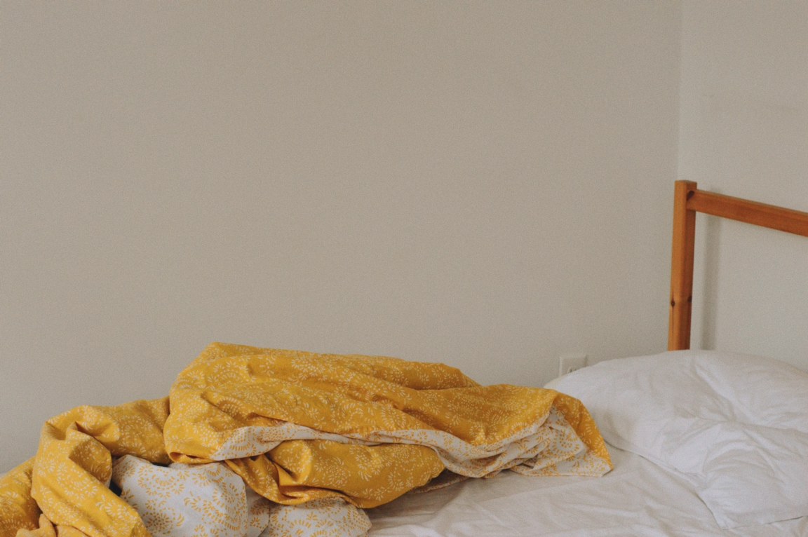 Photo of a bed with white sheets and a yellow duvet on it.