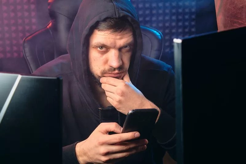 Photo of a man inn a hoodie, sitting in a gaming chair looking devious