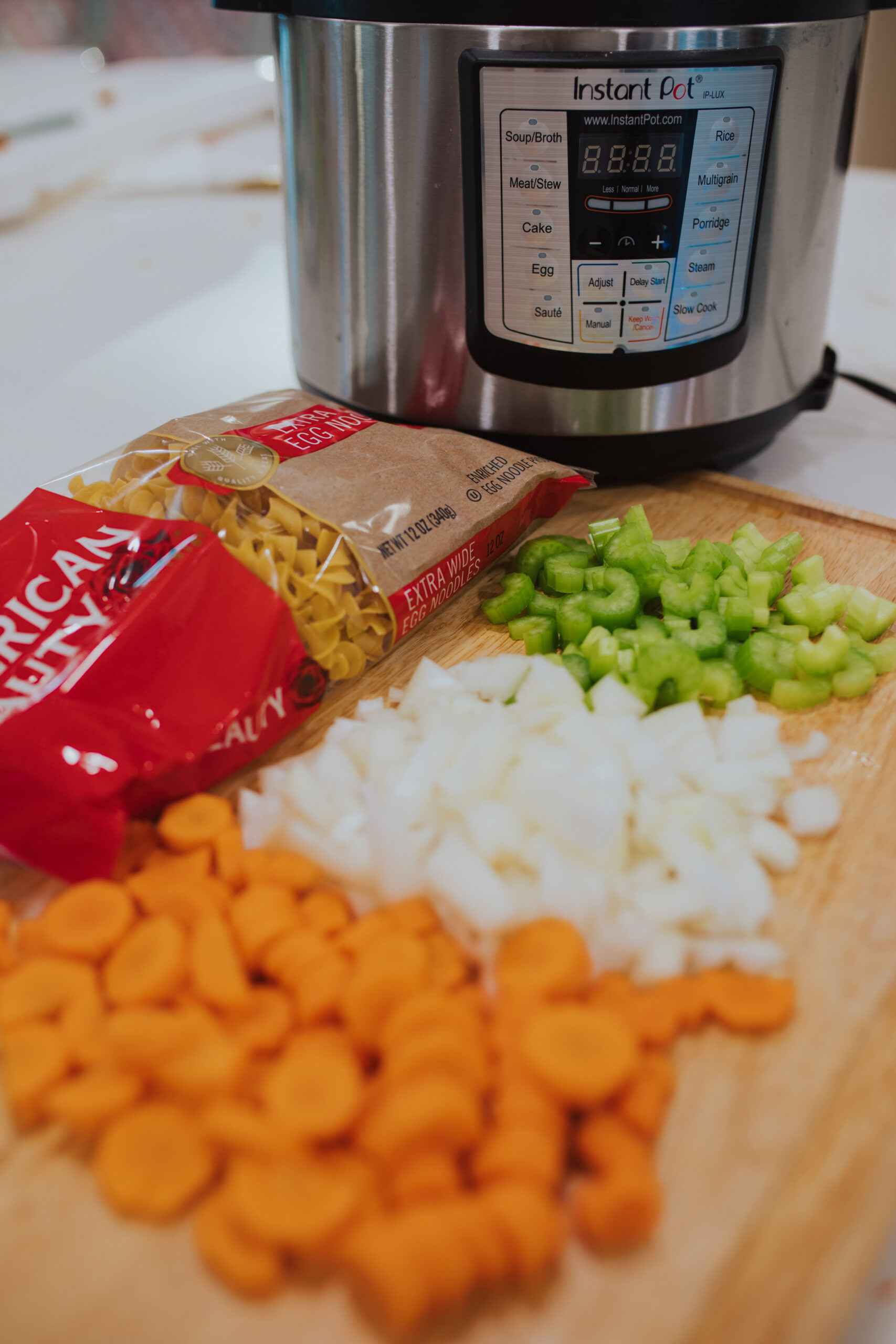 Cutting board with chopped carrots, onions and celery. Packaged noodles in the background. Instant pot in the background.
