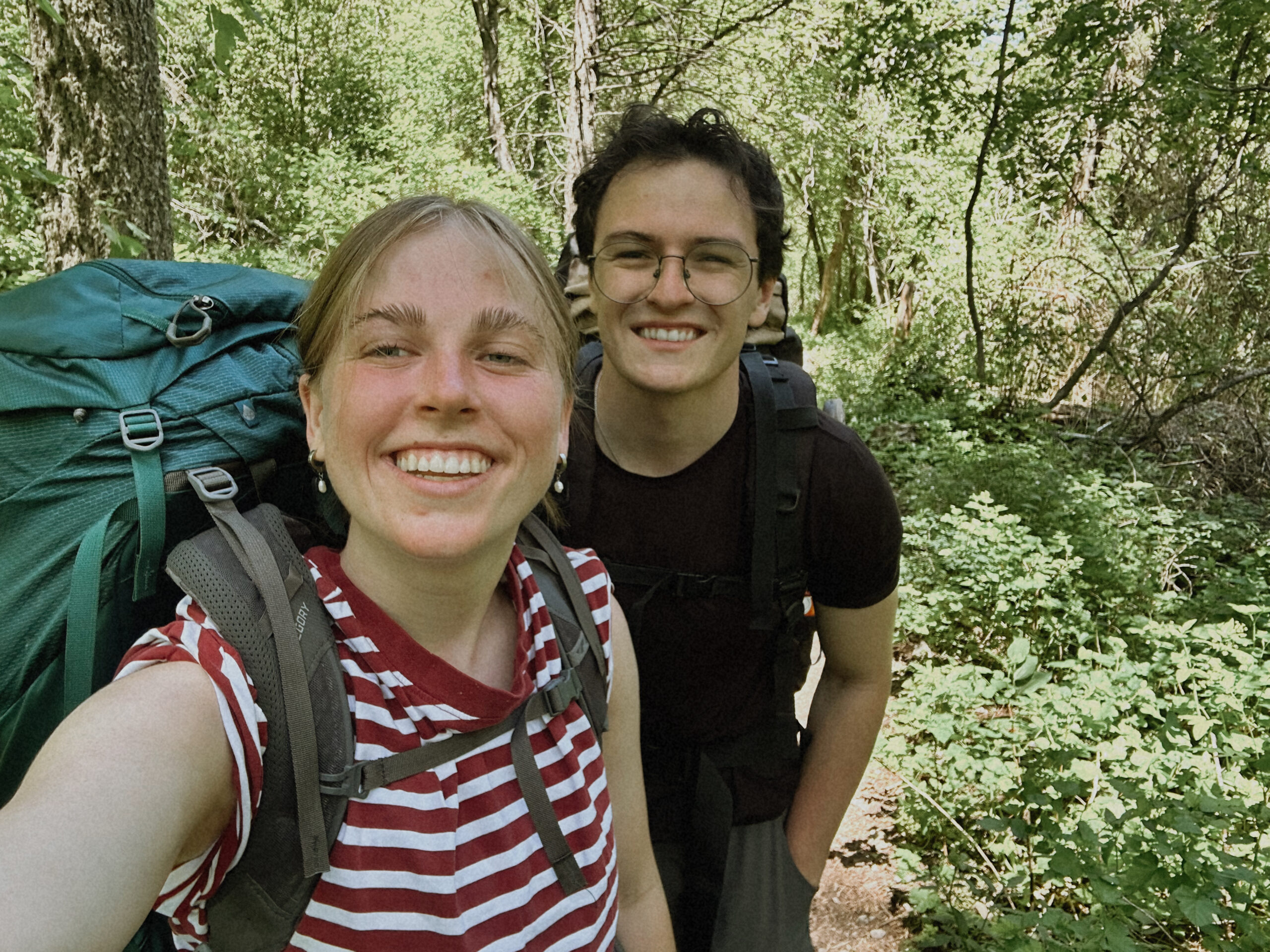 Two hikers with backpacks smiling on a green summer trail