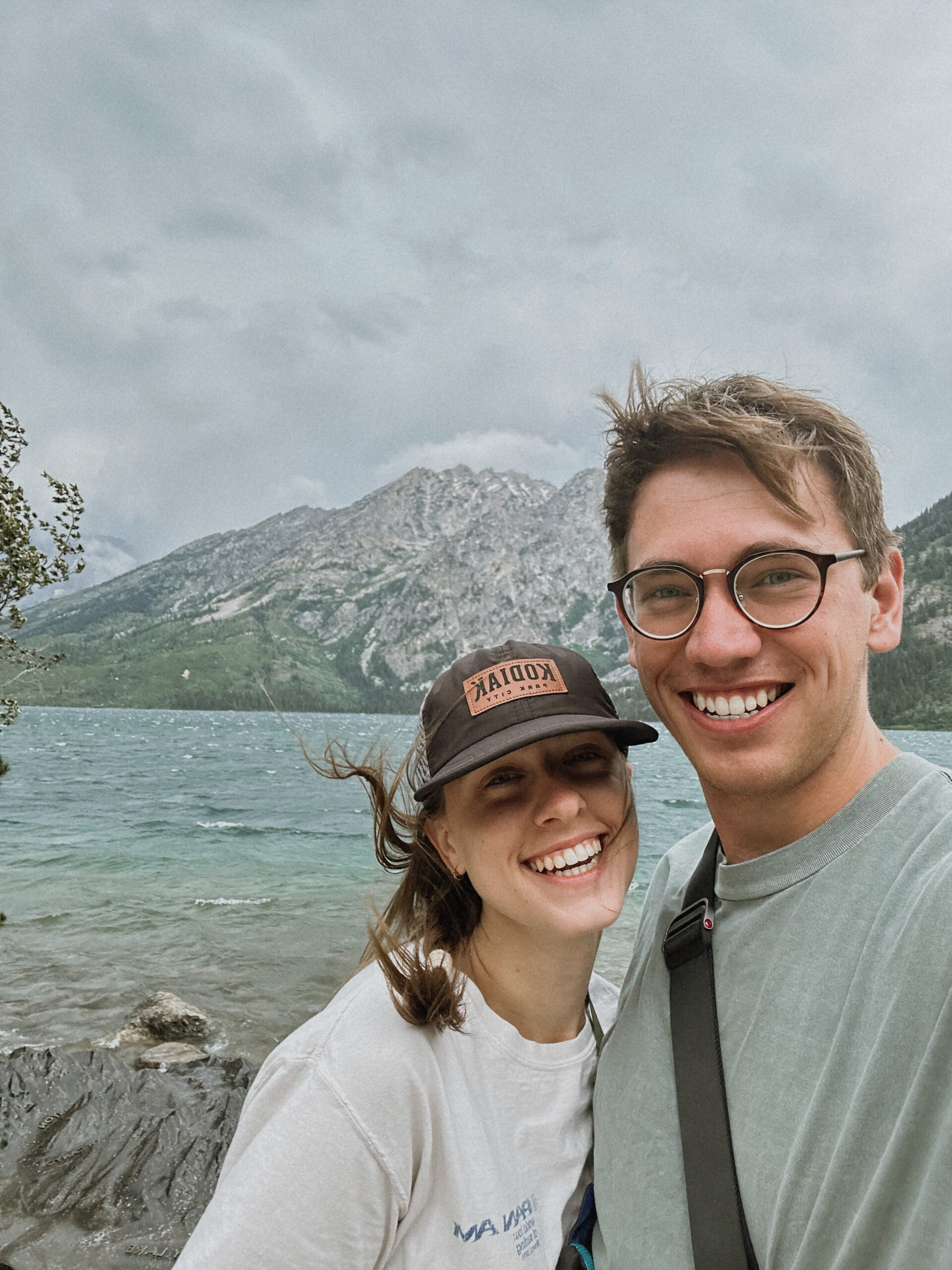 Couple smiling in front of a mountain lake on a summer trip
