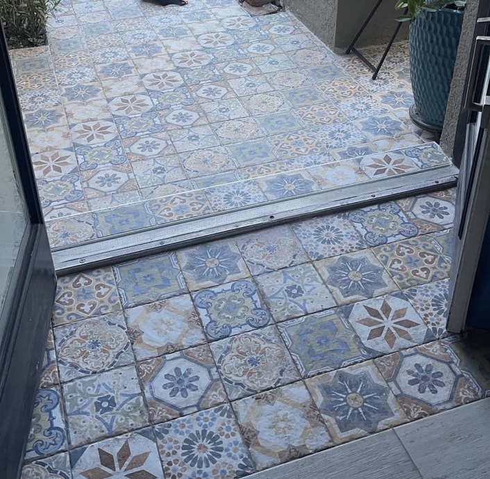 Blue and cream patterned decorative tile at an exterior entry, with a metal threshold strip.