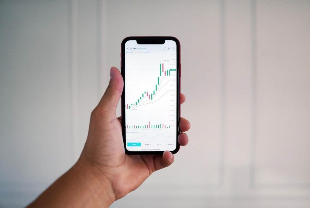 Hand holding a smartphone showing a rising stock chart on a trading app.
