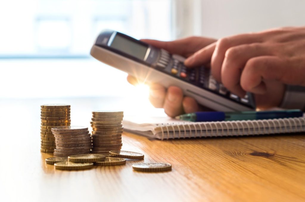 Stacks of Euro coins on a wooden desk with a person using a financial calculator for budgeting.