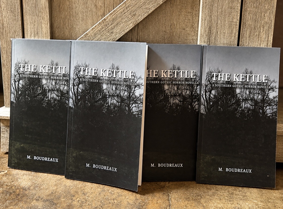 Paperback copies of The Kettle by M. Boudreaux on a wooden surface.