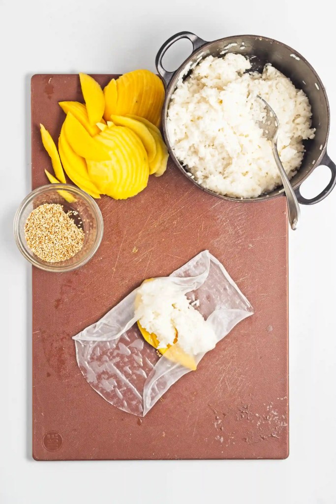 mango and sesame seeds being rolled in rice paper