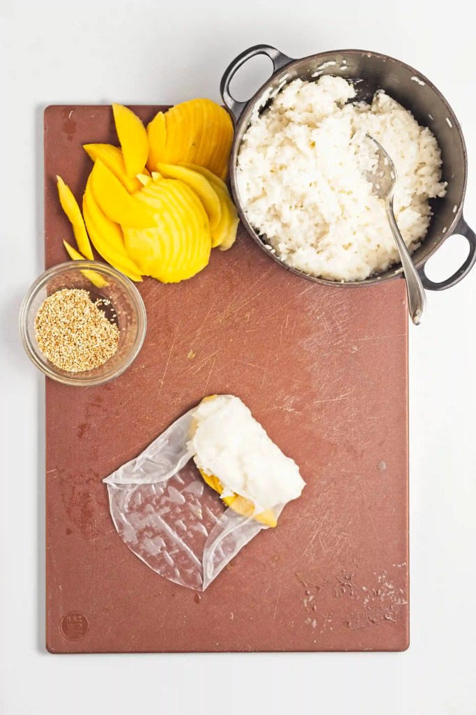 mango and sesame seeds being rolled in rice paper