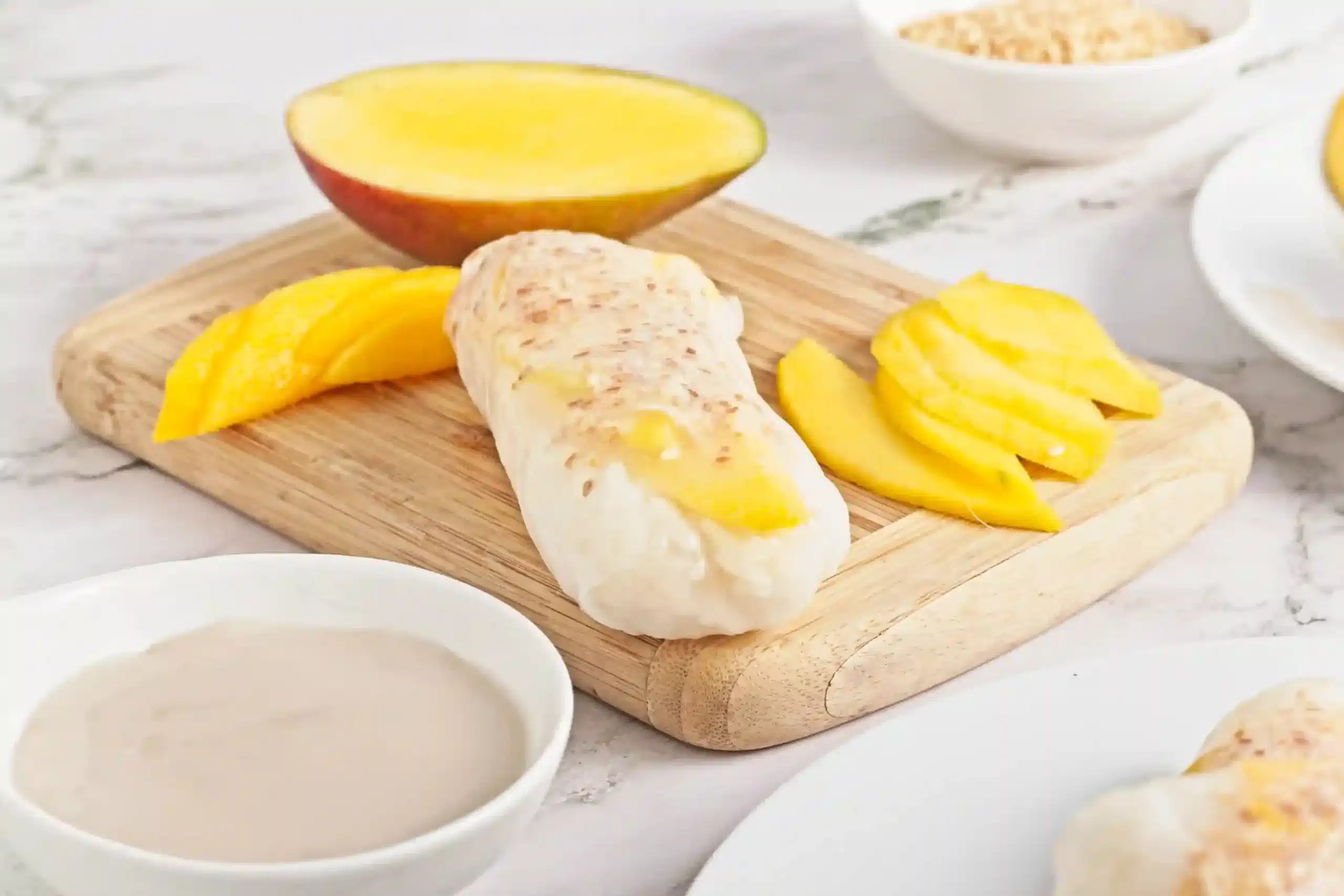 vegan and gluten free mango sticky rice spring rolls on a wooden cutting board next to half a mango