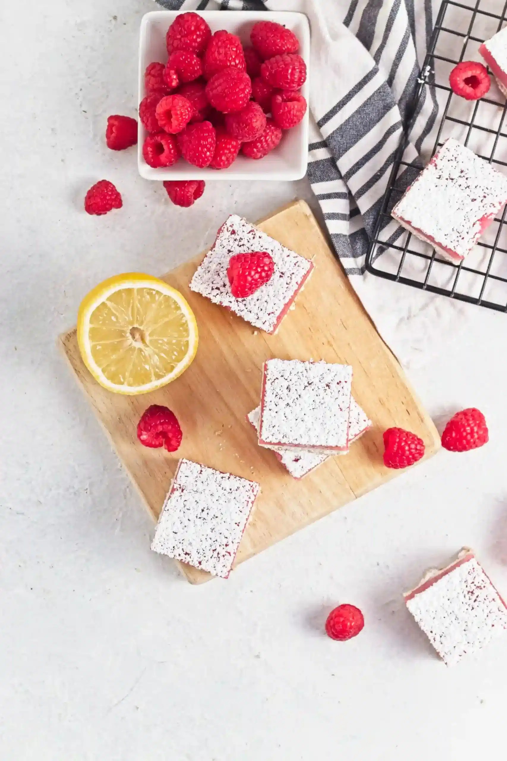 vegan Raspberry Lemon Curd Bars stacked on top of each other on a wooden board with raspberries and lemons around