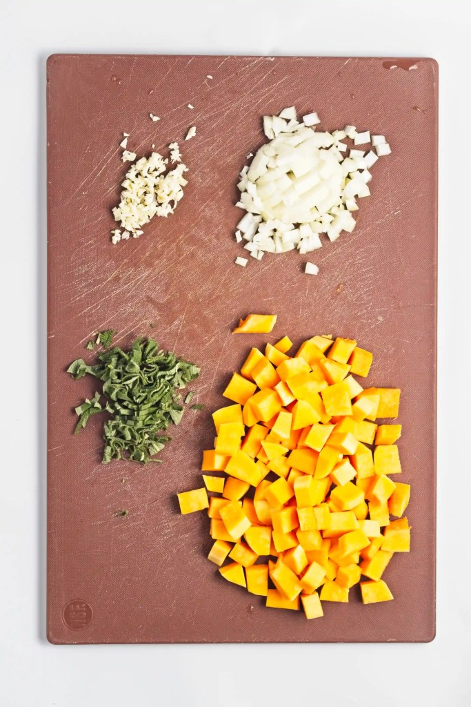 onion, garlic, sage, and butternut squash cut up on a cutting board
