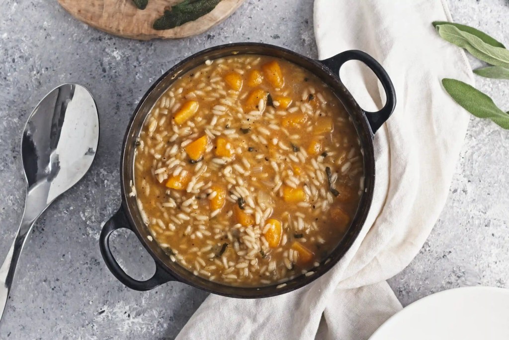 a butternut squash risotto in a black cast iron pan next to a beige napkin