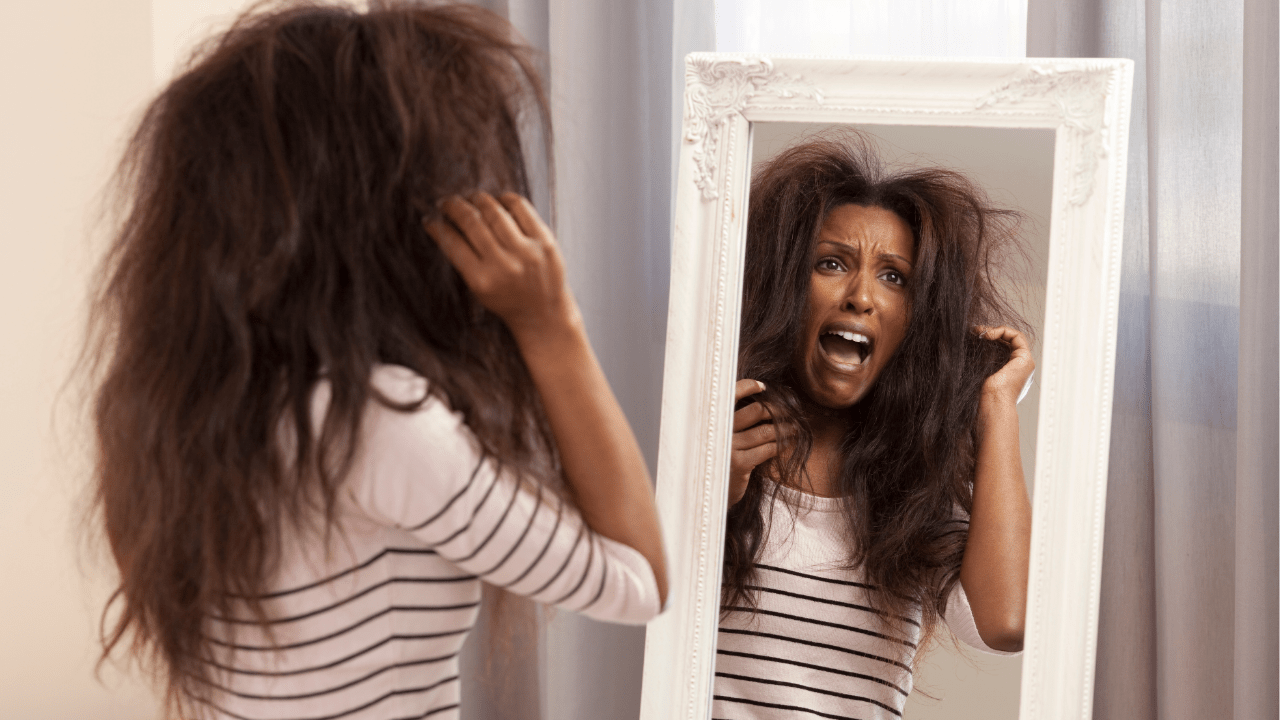 A woman looks at herself in the mirror with a shocked expression, symbolizing a bad day starting with hair problems, highlighting the emotional challenges discussed in the blog.