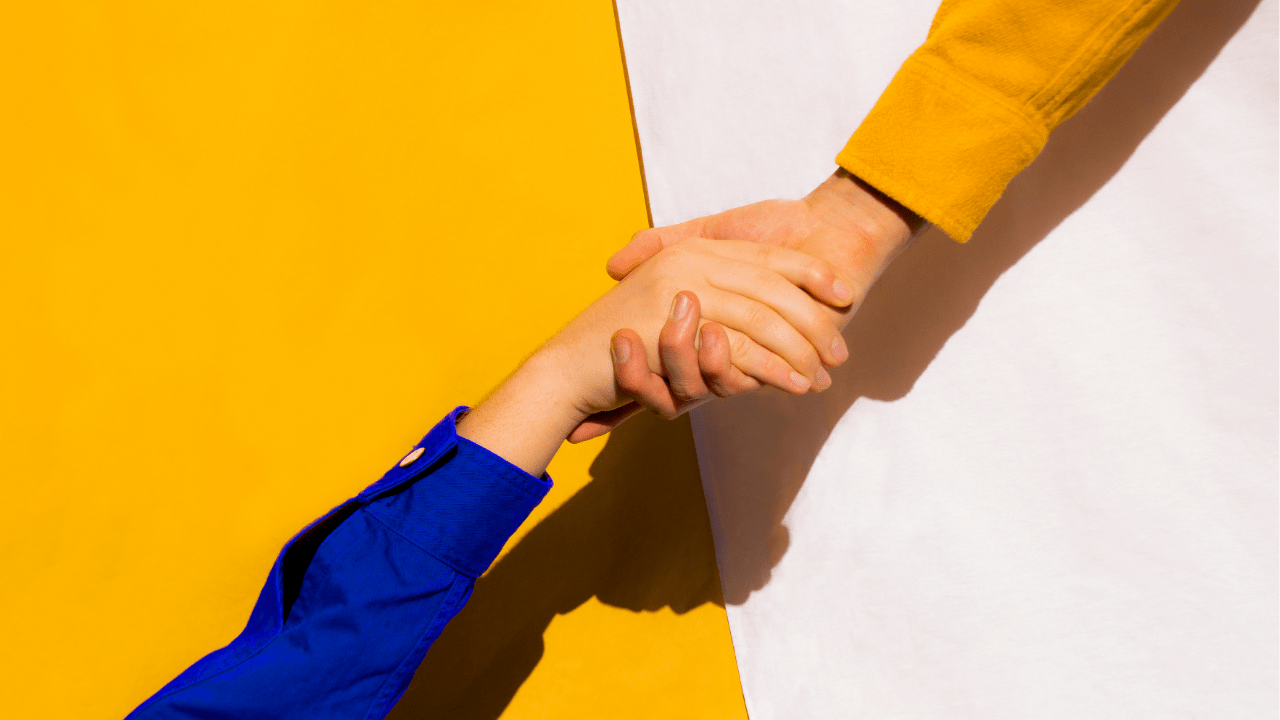 Close-up of two hands clasped together against a vibrant yellow and white background, symbolizing support and connection. This image reflects the essence of the blog post about helping a loved one who is struggling with anxiety, emphasizing the importance of being there for someone in need.