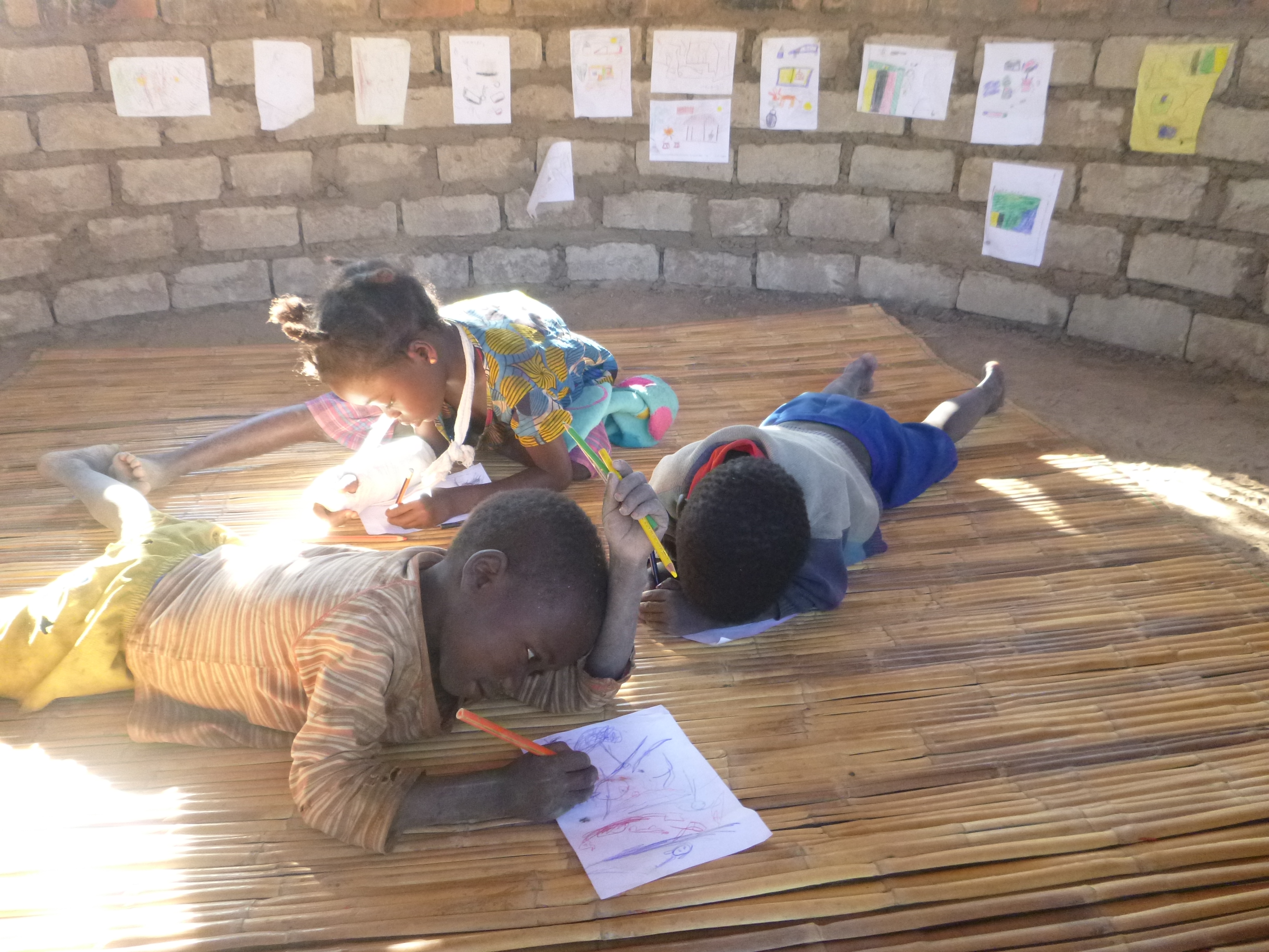 Katongo, Evet, and and Agri drawingin my nsaka. Pictures on the wall are a collection of drawings from all the neighborhood kids.