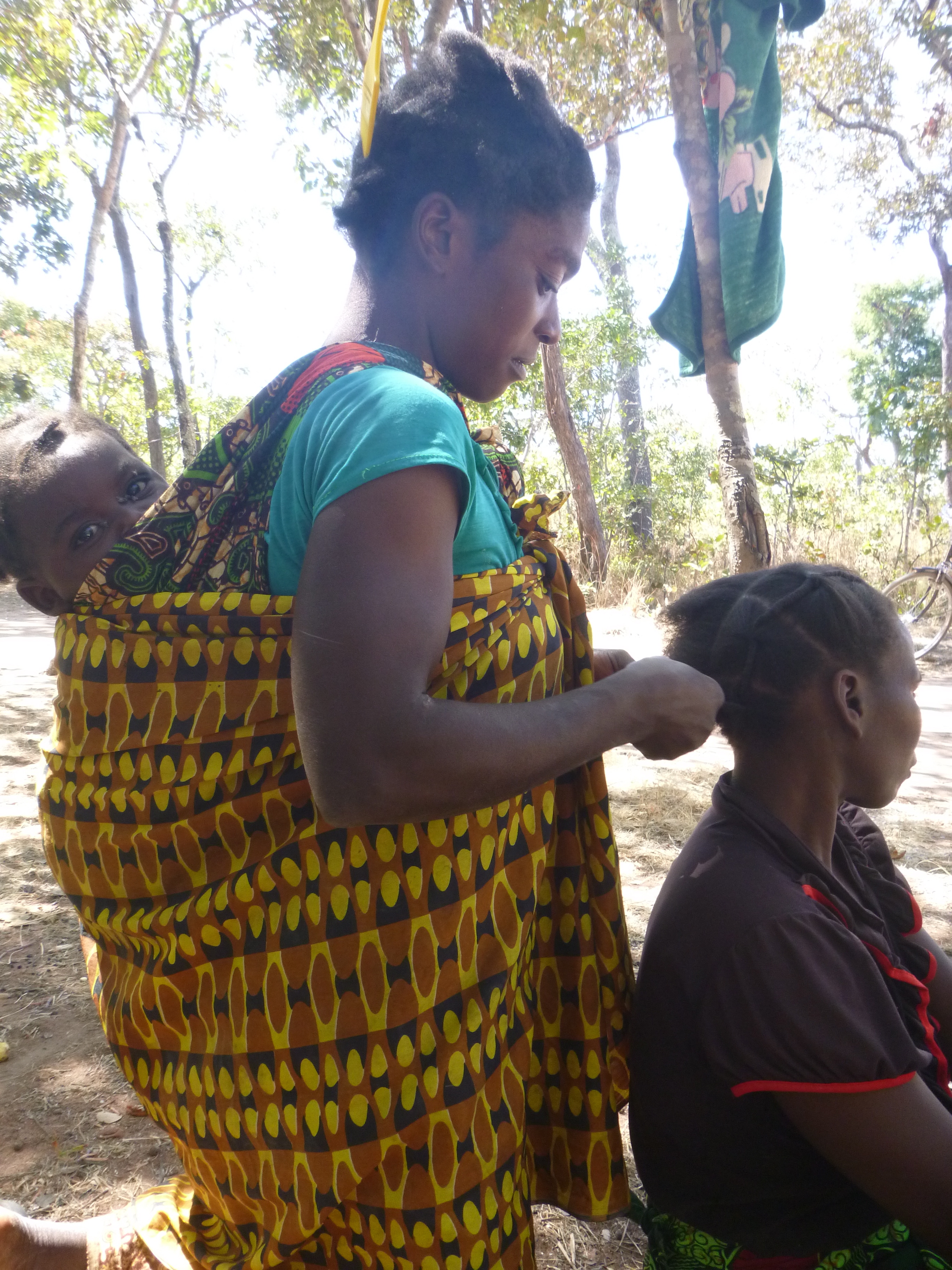 Ba Scolastica braids Ba Agatha's hair while her baby, Musonda, checks out the camerawoman.