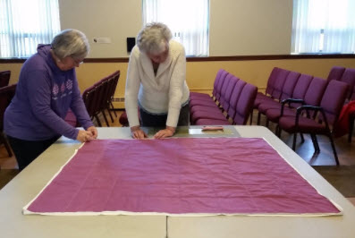 8a. Batting is sandwiched between the quilt top and a fabric backing. Safety pins are used to temporarily tack the three layers together.