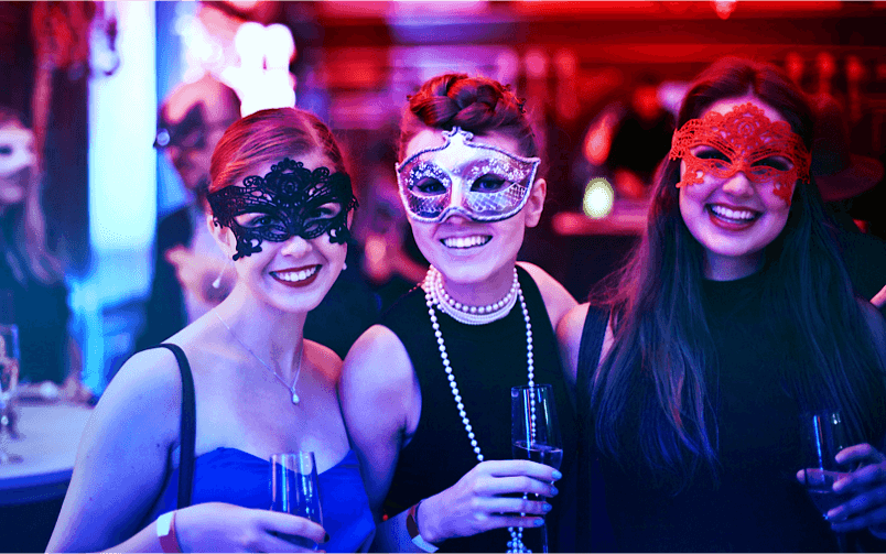 Three women wearing elegant masquerade masks at a festive party.