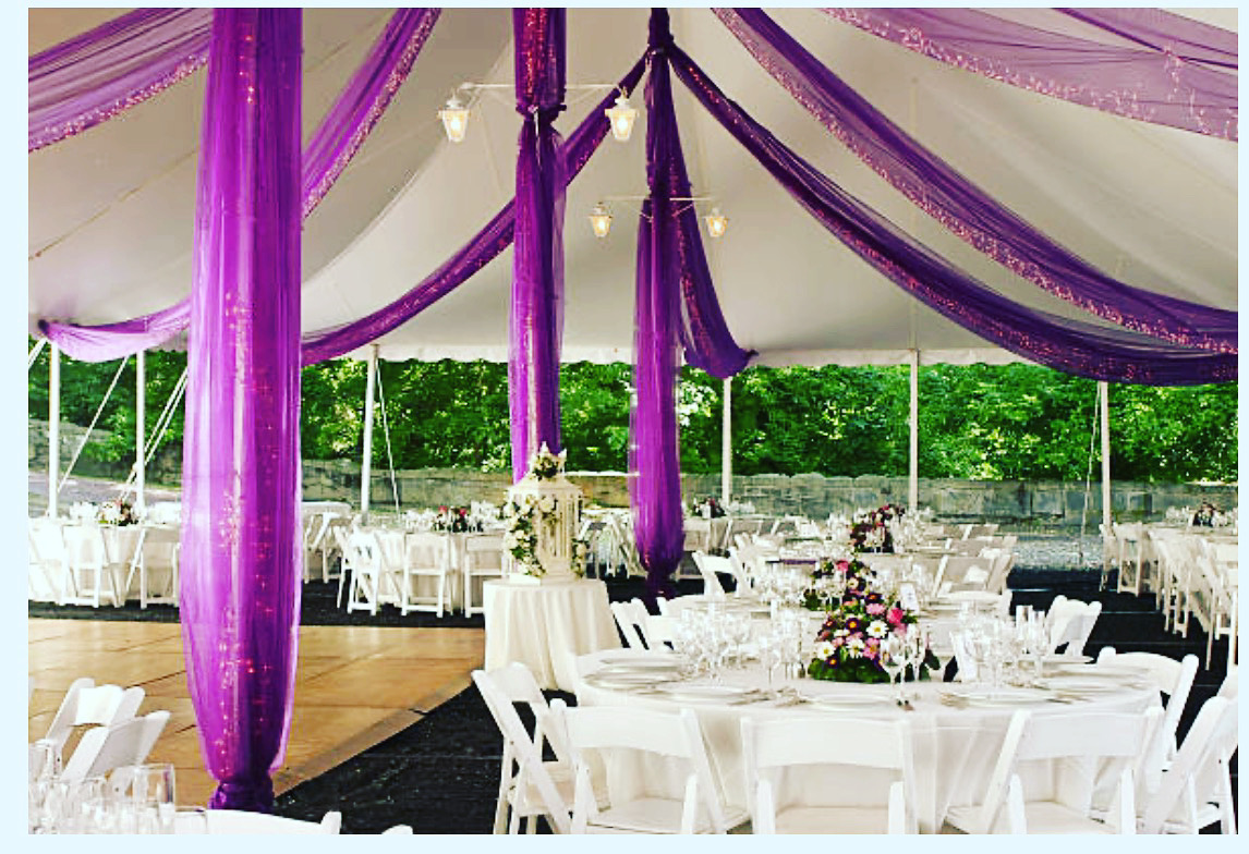 Elegant outdoor wedding reception with white tables and purple drapery.