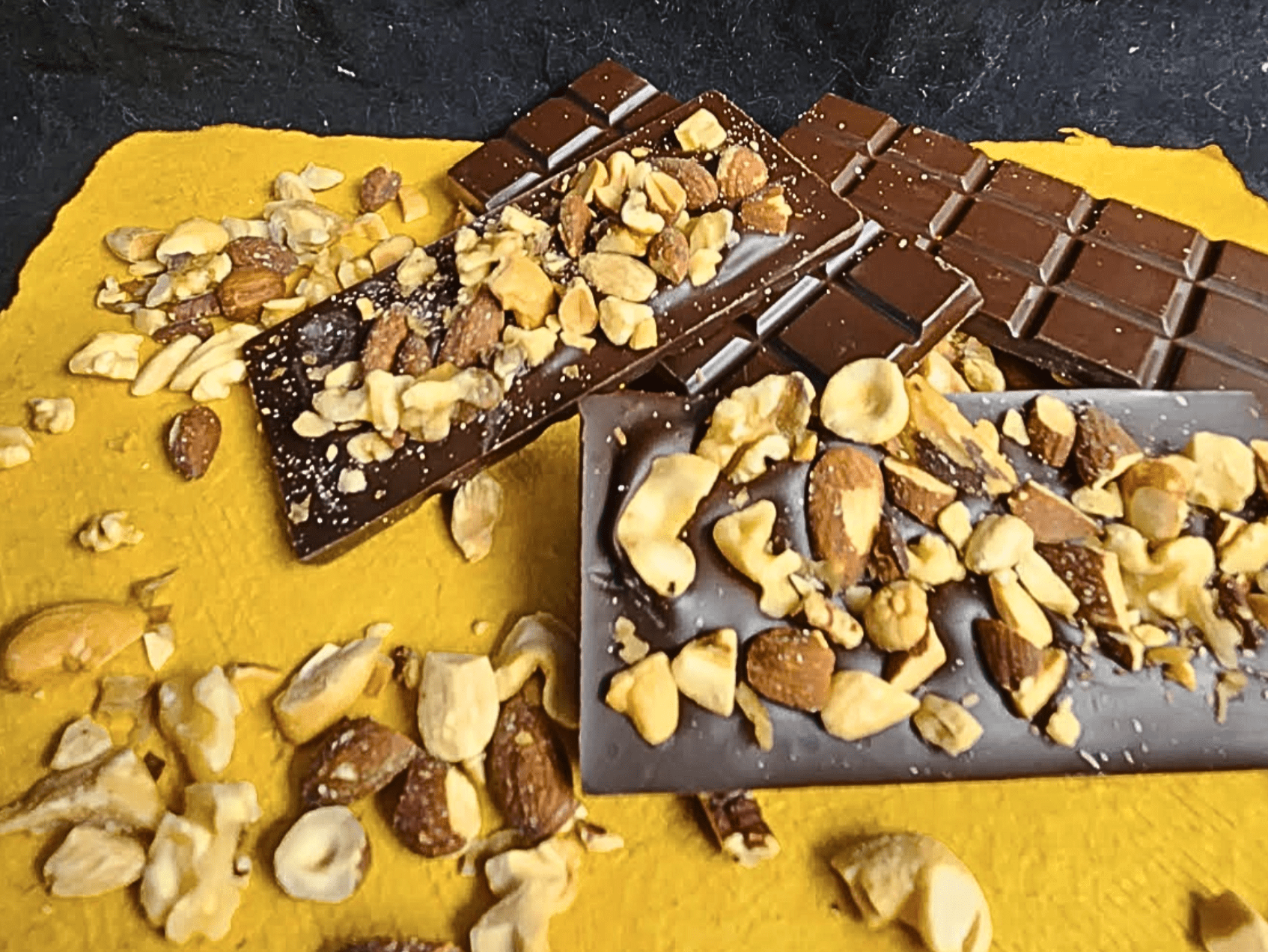 Chocolate bars with chopped mixed nuts on yellow napkin.