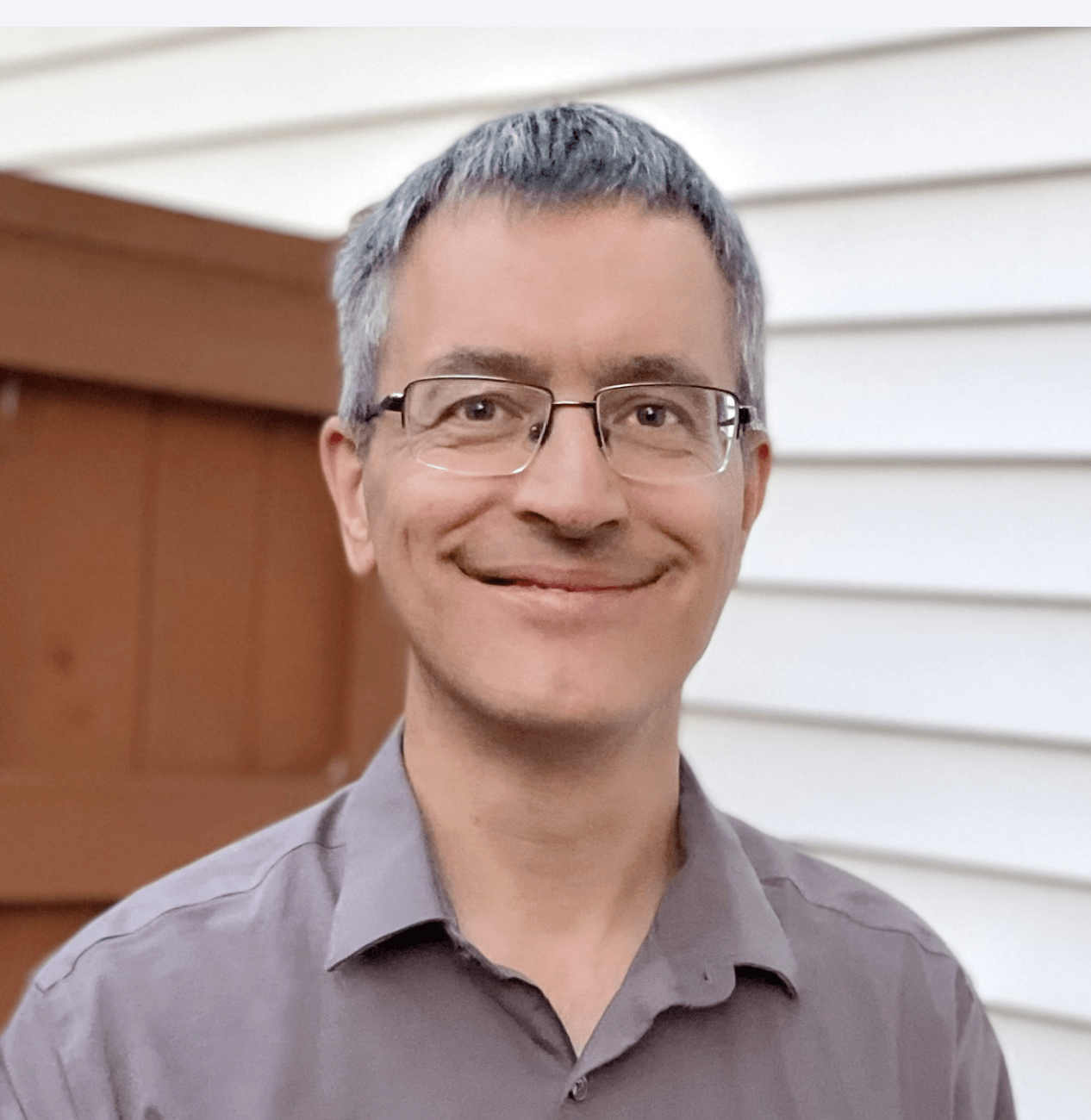 John smiling next to a white house and a brown fence
