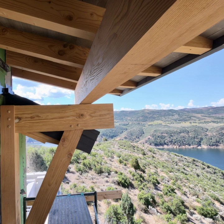 View of a home from under a wooden roof eave showing stained timber framing beams and diagonal support brackets.
