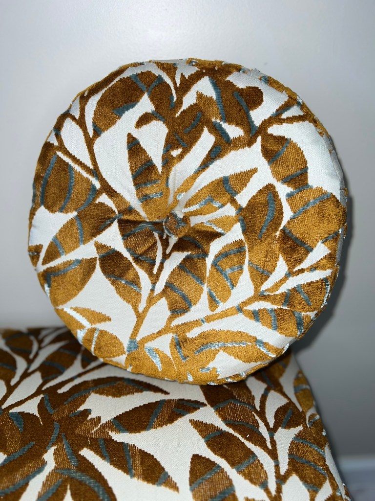 A brassy golden cut velvet fabric with teal accents on a designer botanical print agains t a contrasting ivory background.